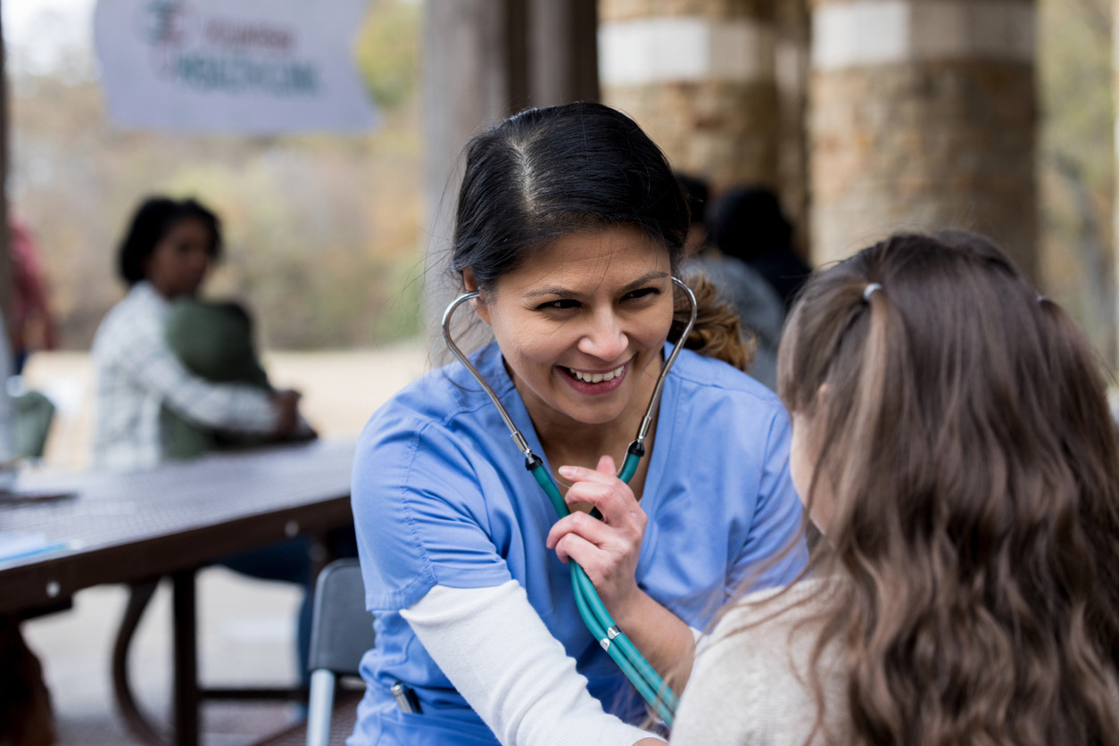 A person with a stethoscope listening to a child Description automatically generated